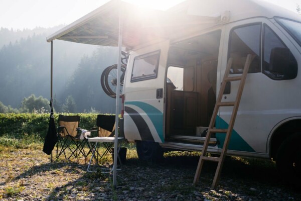 Vintage camper van parked on campground or camping in forest. Beautiful sunny morning in wild camp spot. Nomadic vanlife lifestyle. Relaxed simple vacation. RV camping destination