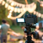 Camera recording standing on tripod with defocused illuminated live music concert event and camping background