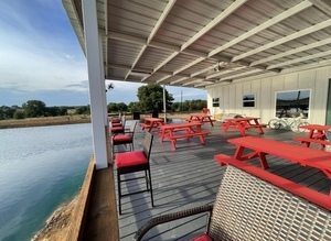 The RV park patio features picnic tables, comfortable chairs around a bar area, and a mounted TV for guests to enjoy.